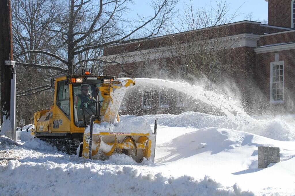 A town sidewalk plow churns through deep snow outside the Acton Free Public Library. Photo: Dakota Antelman/The Acton Bridge