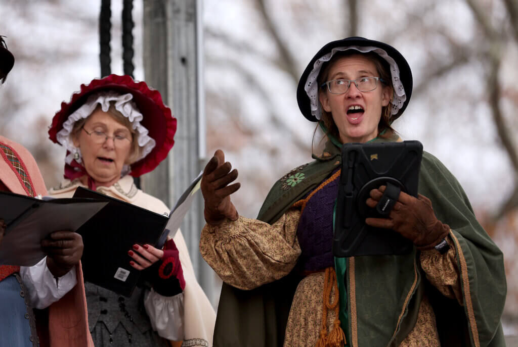 Acton Players musical director Kathryn Denney, right, leads her choir in Christmas carols on the main stage during Acton’s annual Tree Lighting on Sunday, December 7, 2025. Ken McGagh/The Acton Bridge