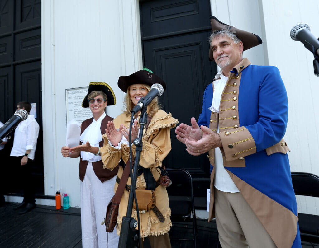 Rob Morrison of Acton, right, Mara Dolan of the Governor’s Council, and Jennifer Hurley-Wales of Acton Indivisible applaud after Concordians voted to accept the Declaration of Independence during “Declaring Independence Then and Now In Acton” on the steps of the First Parish in Acton on Saturday, July 11, 2026. The event was sponsored by the Wright Tavern. Ken McGagh/The Acton Bridge