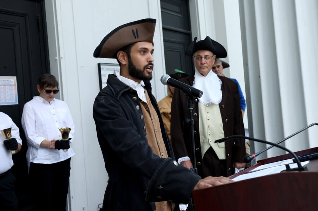 Ravi Simon of Sudbury, candidate for Massachusetts legislature, delivers his portion of the Declaration of Independence as Tom Wilson, right, of the Wright Tavern Legacy Trust look on on the steps of the First Parish in Acton on Saturday, July 11, 2026. Five community members took turns reading sections of the historic document. Ken McGagh/The Acton Bridge