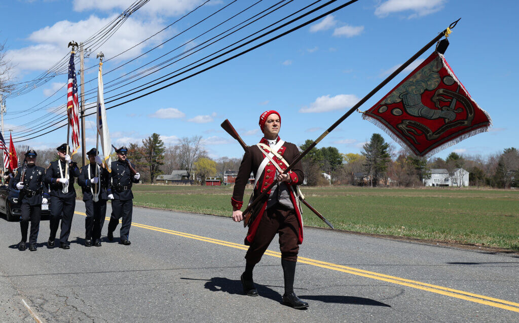 Mark Bailey of the Bedford Minutemen, as the cornet (flag-bearer), carries the Bedford Flag, followed by the Acton Police Honor Guard.
