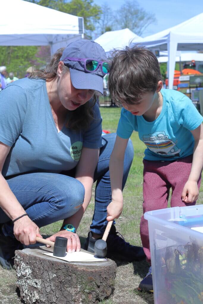 Amanda Benyo of Kids Naturally shows Leo Collins, 4, how to make “smash art” with flowers. The flowers, when hit between papers, leave a pattern. Photo: Trace Salzbrenner/The Acton Bridge