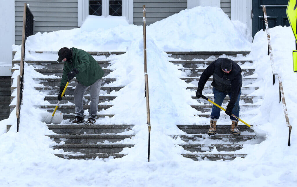 Jim Seaver, left, and Gary McKeon clear snow outside St. Bernard’s Catholic Church in Monument Square. Photo: Ken McGagh/The Acton Bridge