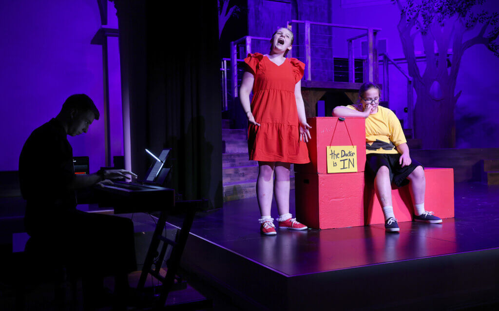 Madeleine Kagels, center, as Lucy, and Charlie Brown, (Madeleine Kagels) perform the classic “The Doctor Is In” scene during the Acton Youth Theatre Summer Stock Troupe production of “You’re A Good Man Charlie Brown” on Thursday, July 23, 2026. Ken McGagh/The Acton Bridge