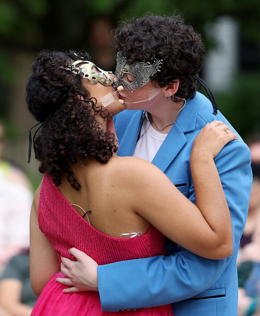 Shakespeare's timeless tragedy gets a 1980's reimagining Sara Gluck as Romeo, right, and Eliza Zangerl as Juliet kiss during the masquerade ball scene during the Acton Players presentation of William Shakespeare’s “Romeo And Juliet” at the Acton Free Public Library lawn on Saturday, August 1, 2026. Sara Gluck, 21, of Billerica, is a rising senior at Salem State University. Eliza Zangerl, 22, of Waltham is a 2026 Harvard graduate. Both leads are first-time performers for Acton Players. Ken McGagh/The Acton Bridge
