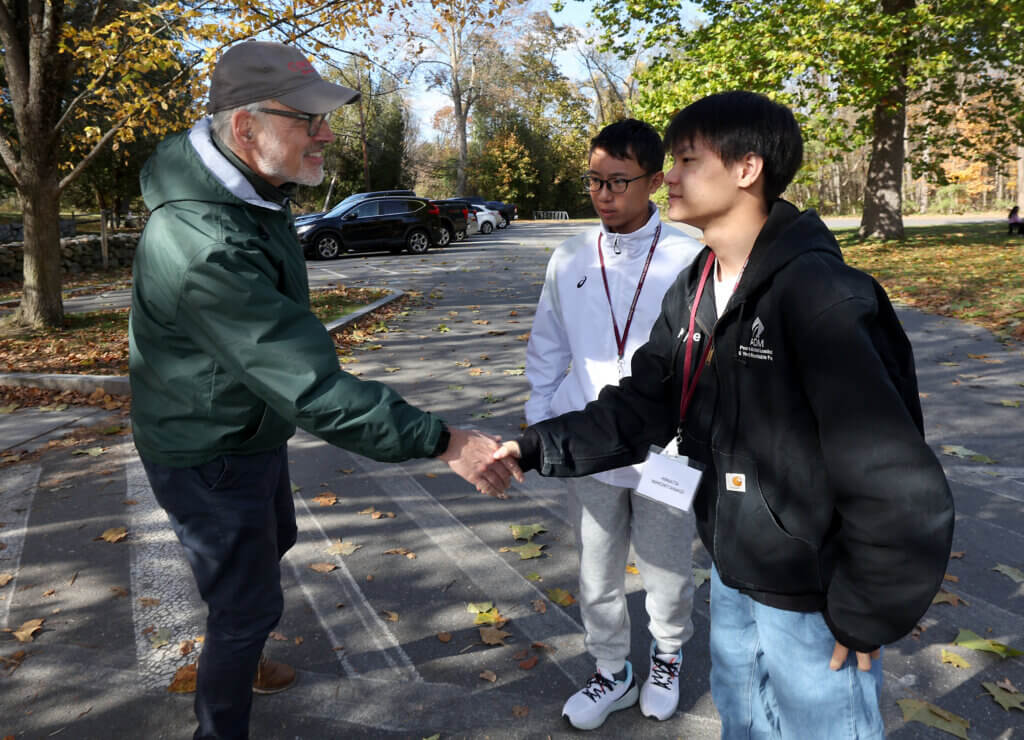 Tour guide Joe Palumbo shakes hands with Nanae student Hinata Nihonyanagi at North Bridge on Tuesday, October 28, 2025. Hinata is one of nine students from Japan visiting Acton this year. Ken McGagh/The Acton Bridge