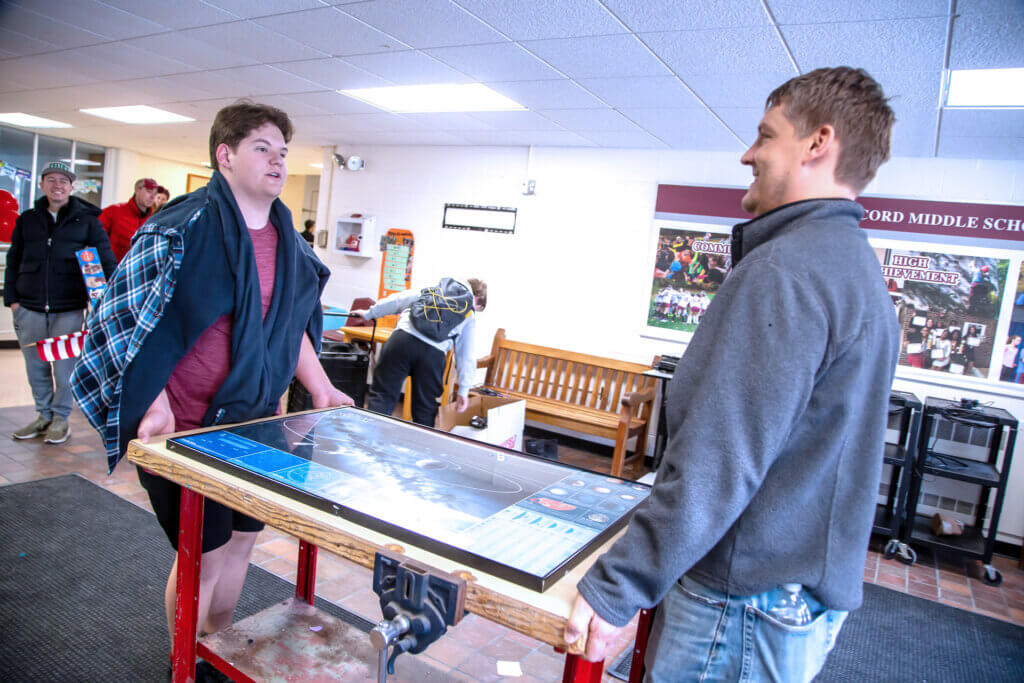 Nate and Jason Reed carry a table through the lobby of the Sanborn school. Photo: Stephen Beyer/The Acton Bridge