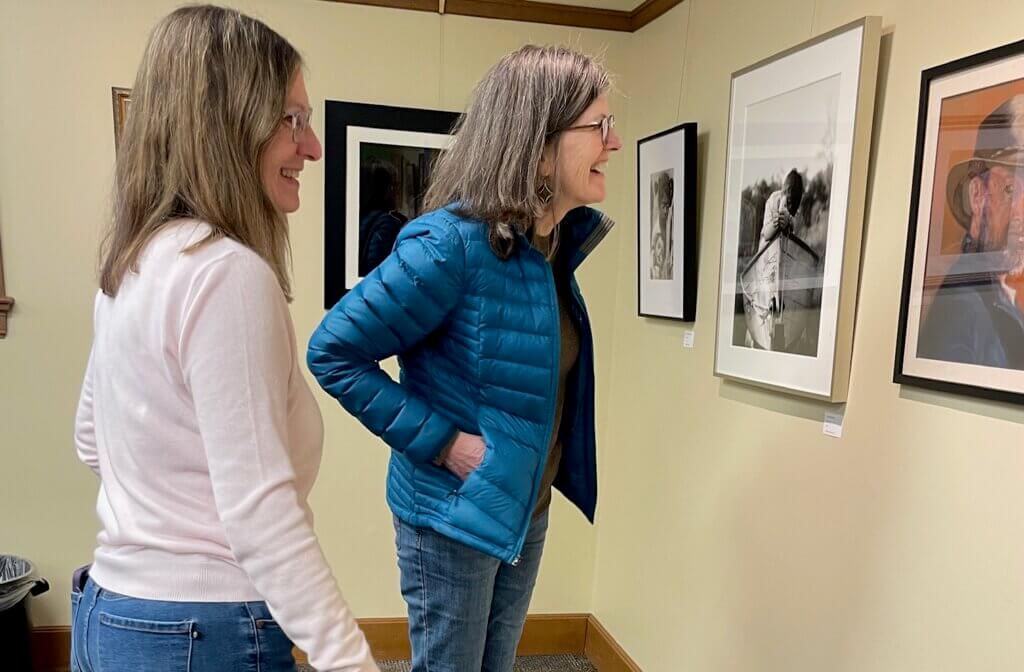 Artist Marcia Schloss (left) and Michele Pruett (right) checking out ArtScape artist Suzanne Revy’s photo of her son, titled “The Boat,” and Dianne Levine’s portrait of her husband, titled “Mark’s New Hat.” Courtesy photo