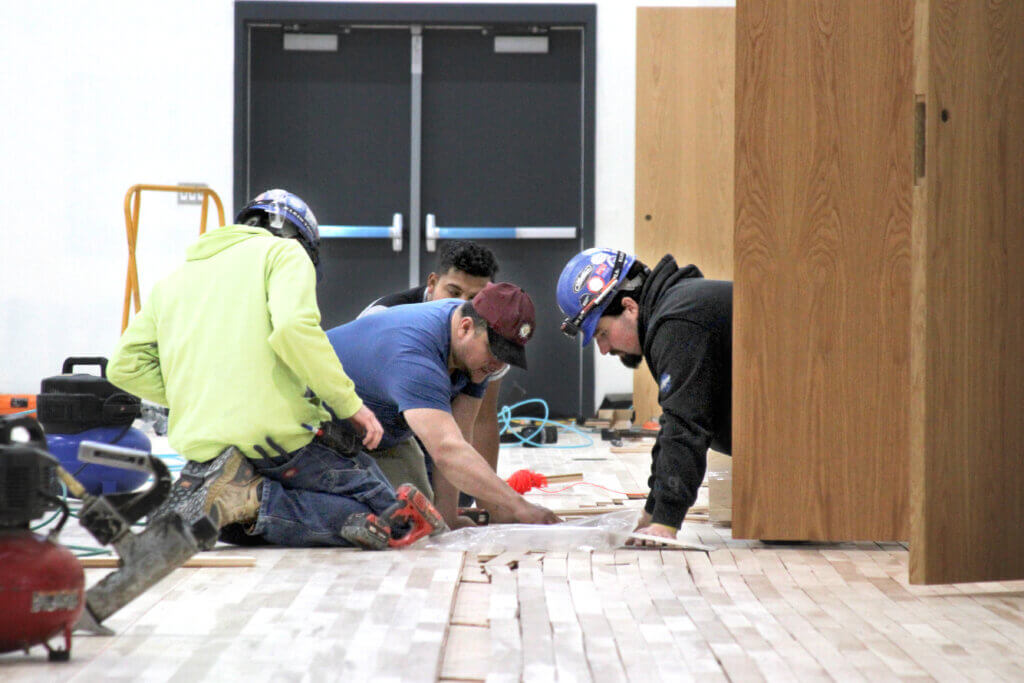 Workers finish laying out the gym floor. Photo: Dakota Antelman/The Acton Bridge