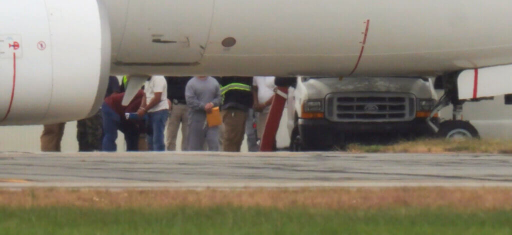 An advocate’s photo shows people in handcuffs beside a waiting plane at Hanscom Field. Courtesy photo