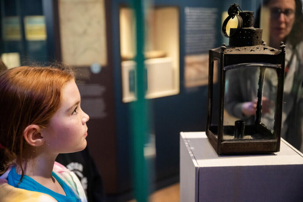 A young visitor at the Acton Museum studies an original lantern used as a signal during Paul Revere’s famed midnight ride. Photo by Mike Ritter