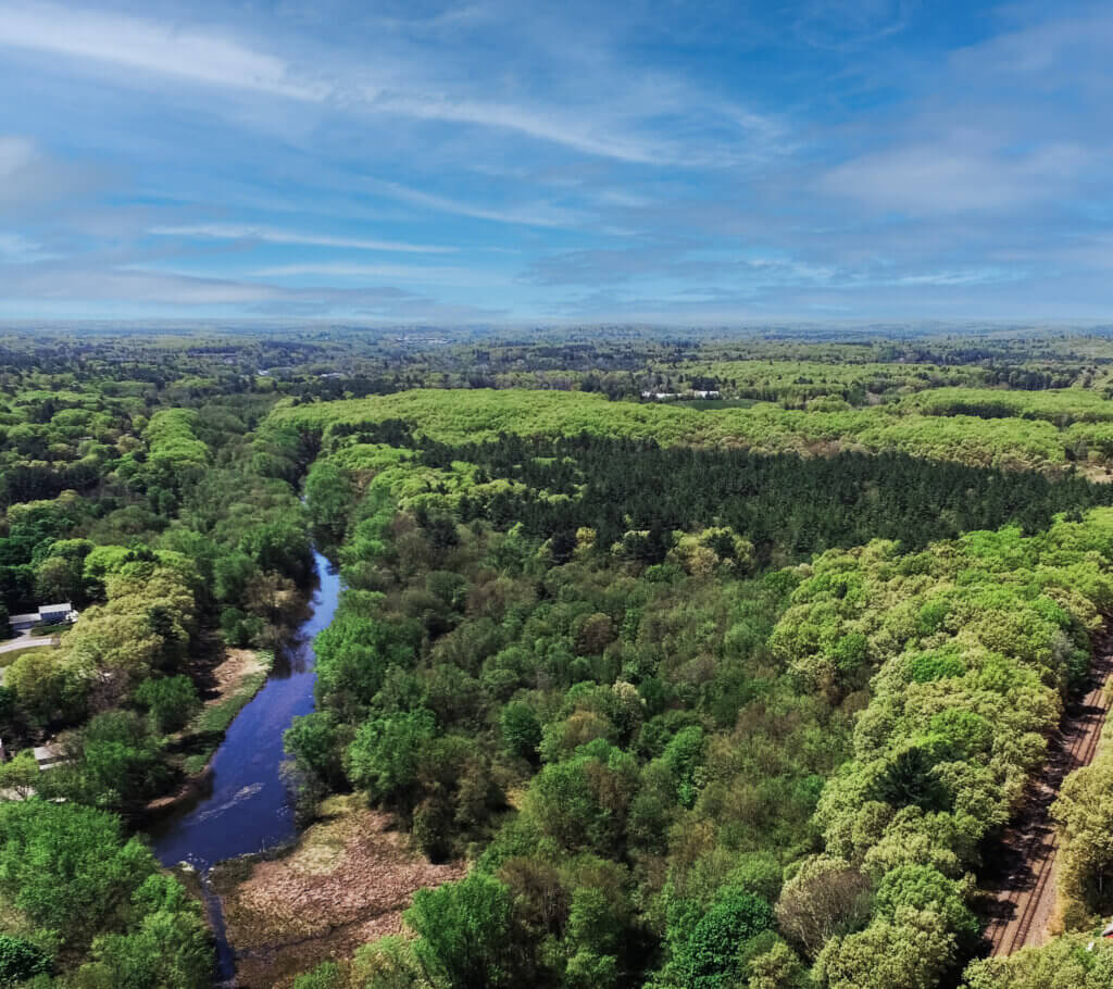 An aerial view shows wooded land at 0 Pond Lane between the Assabet River and MBTA train tracks. Image courtesy O'Brien Commercial Properties
