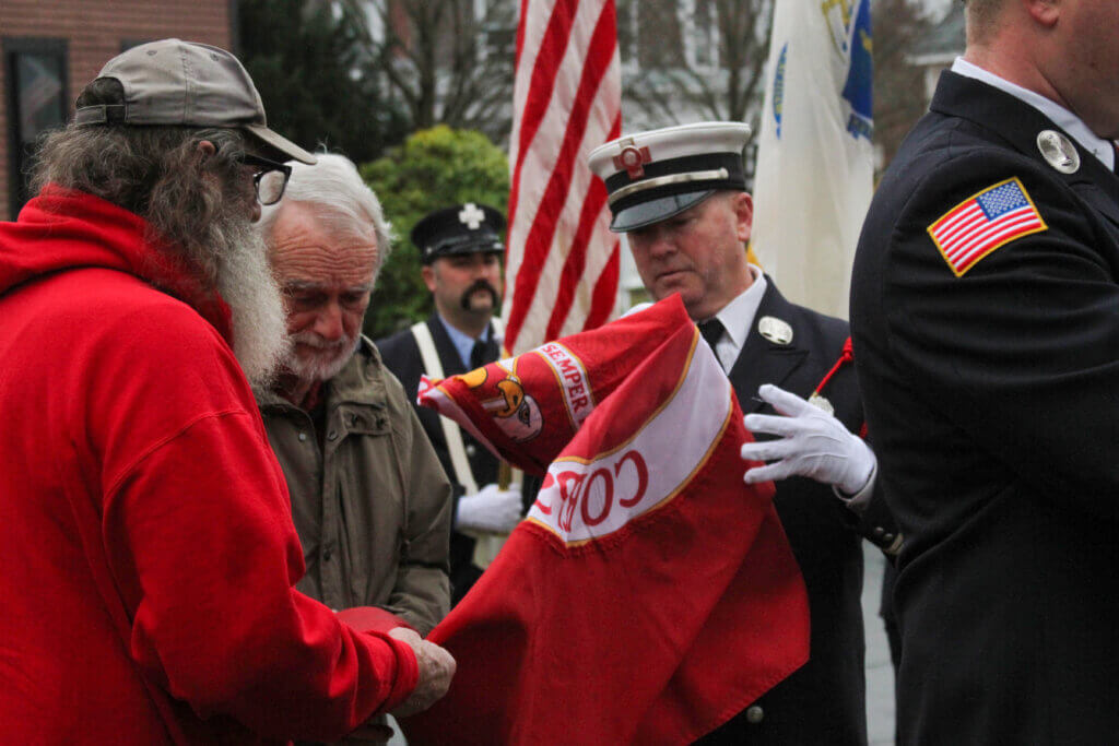 Veterans Bob Recco, left, and Leo Carroll, center, help Fire Capt. Sean Murphy unfurl the Marine Corps flag in Acton Center.
