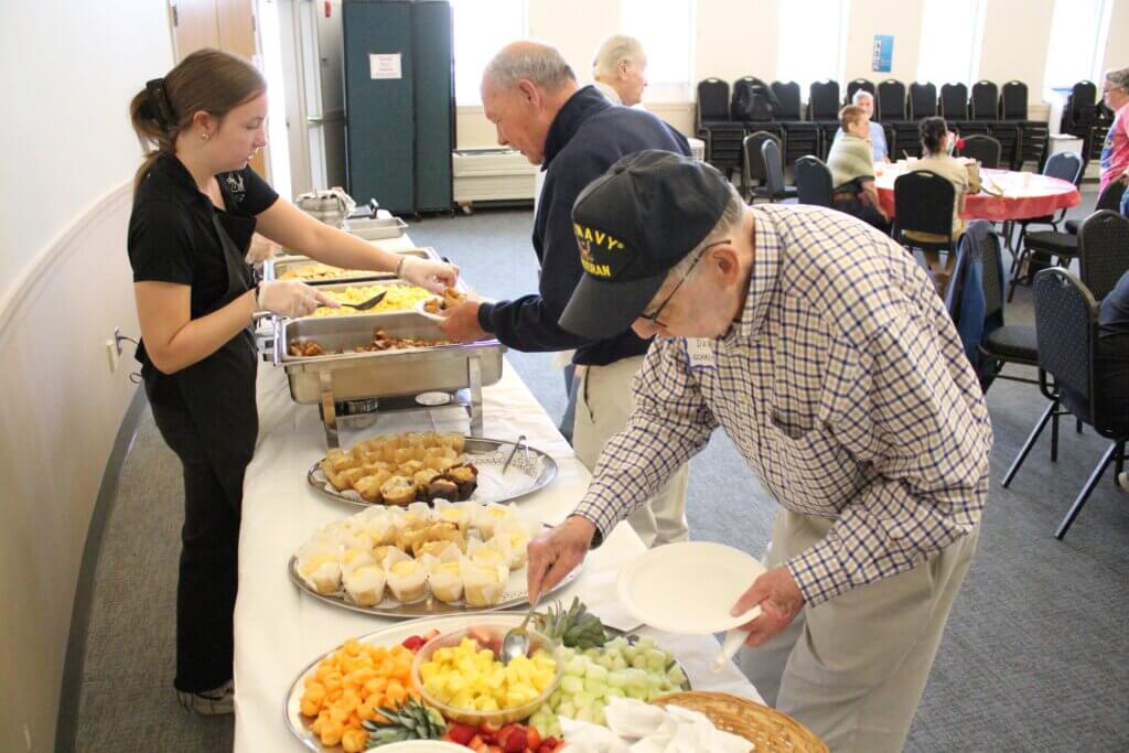 Dave Schaefer, wearing a Navy veteran hat, dishes up fruit during a Memorial Day Breakfast last week. Photo: Dakota Antelman/The Acton Bridge