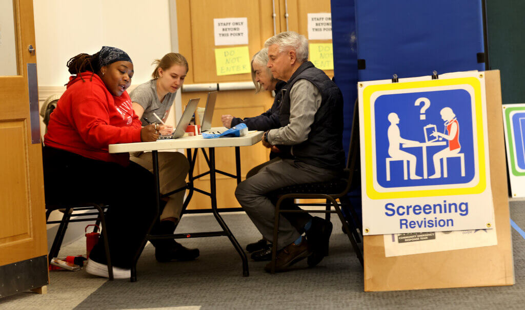 Andrea Joseph, front left, Acton’s public health inspector, and Katie Stanislawzyk, left rear, the town’s public health nurse, perform a simulated health screening of Donald and Claire Moir, right. Photo by Ken McGagh/The Acton Bridge