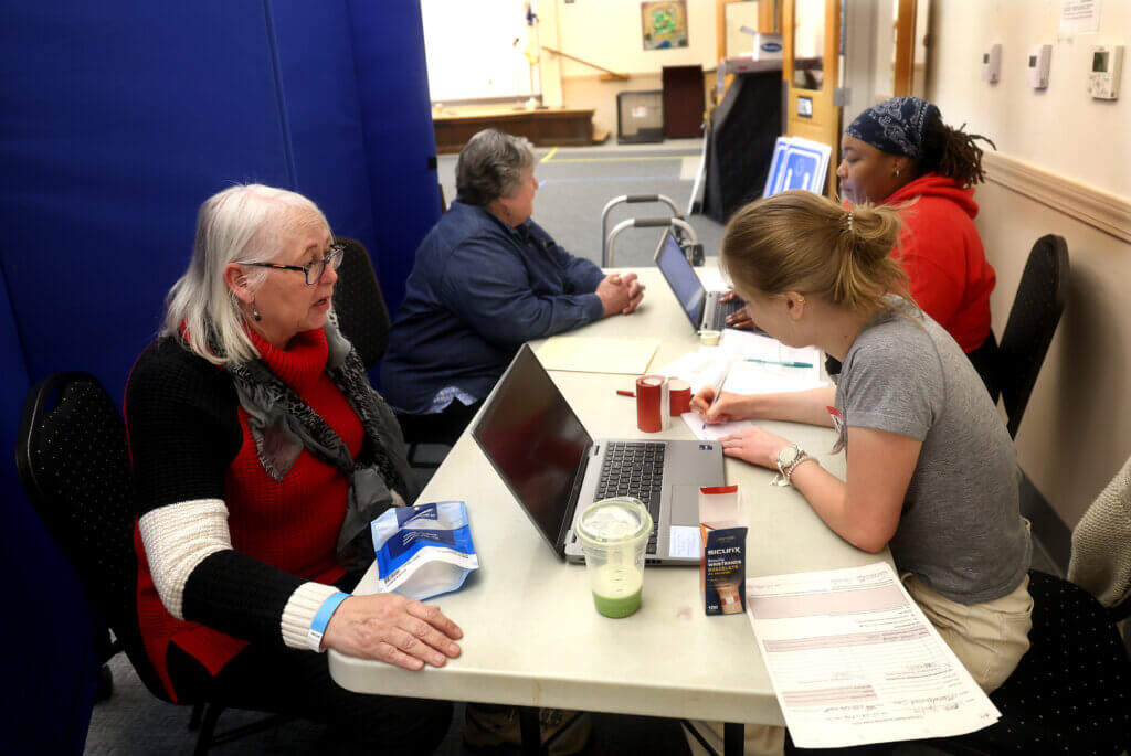Karlen Reed, left, acting as a shelter-seeker, sits for a medical screening with Katie Stanislawzyk, right, the town’s public health nurse. In the rear is Ione Nauseda, left, a volunteer shelter-seeker, and Andrea Joseph, the town’s public health inspector. Photo by Ken McGagh/The Acton Bridge