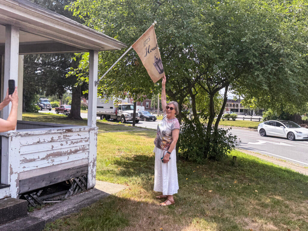 Sandra Conn reaches for a banner flying from the porch of the Cuming House. Photo by Sarah Johnson