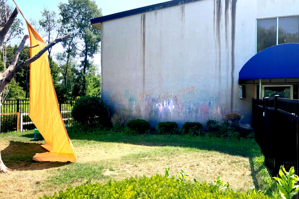 A rainbow of chalk-drawn names and pictures marked the wall beside a former children’s play area. Photo: Dakota Antelman/The Acton Bridge